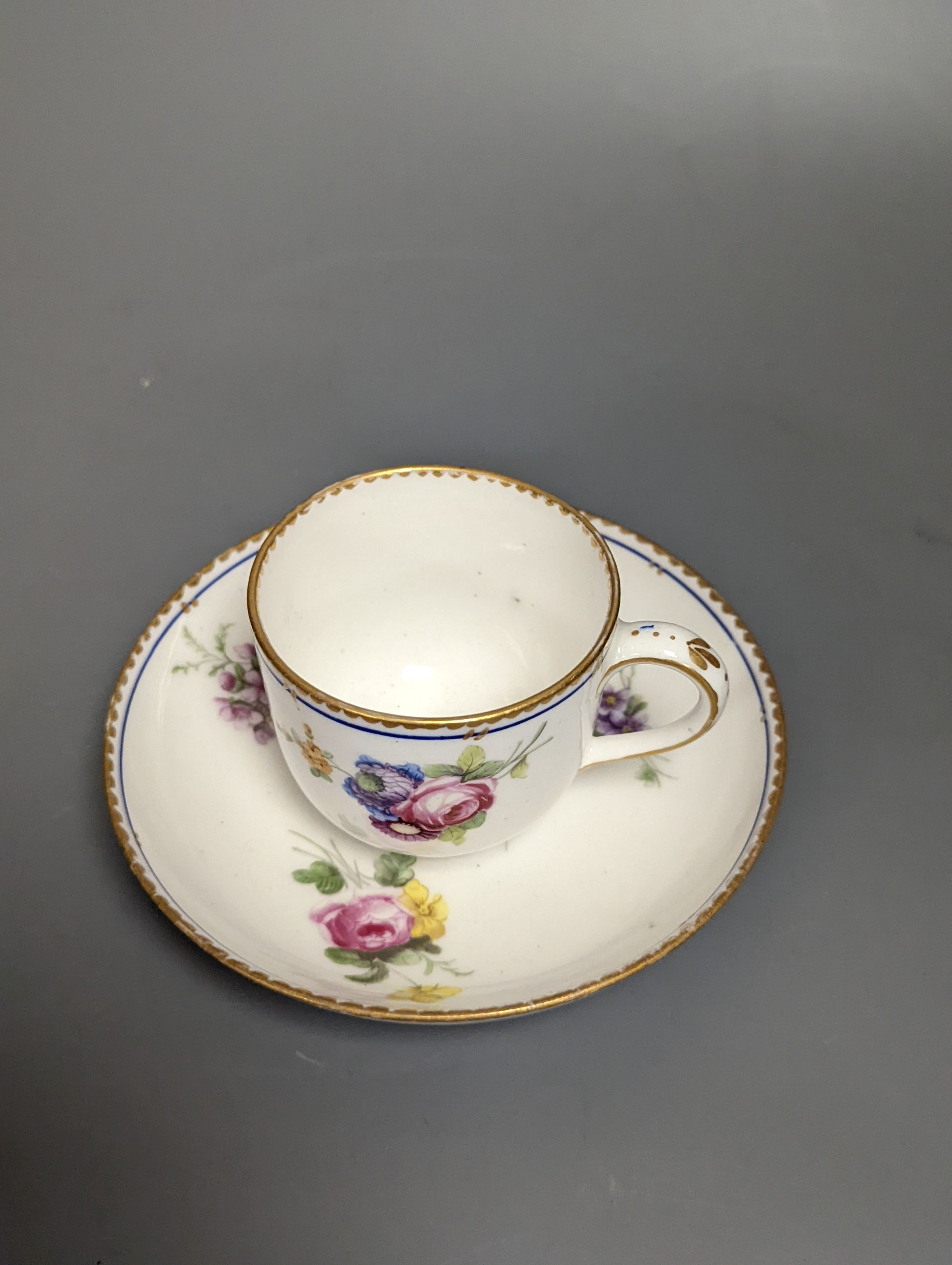 A Sevres coffee cup and saucer painted with floral bouquets under a dentil gilt and blue line border, date code 